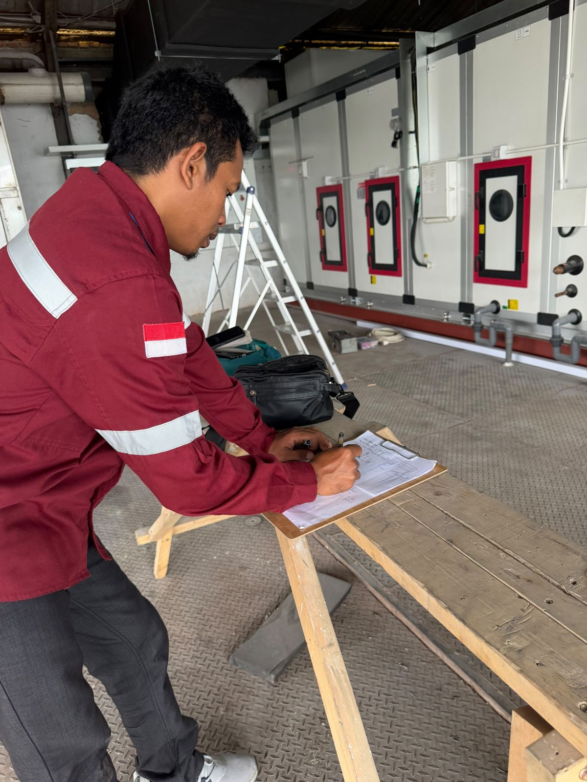 Teknisi mencatat checklist inspeksi di depan deretan AHU